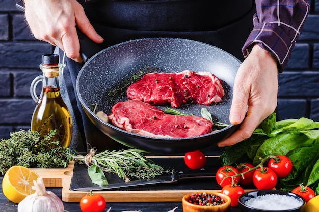 El chef sostiene una sartén con filetes de carne cruda