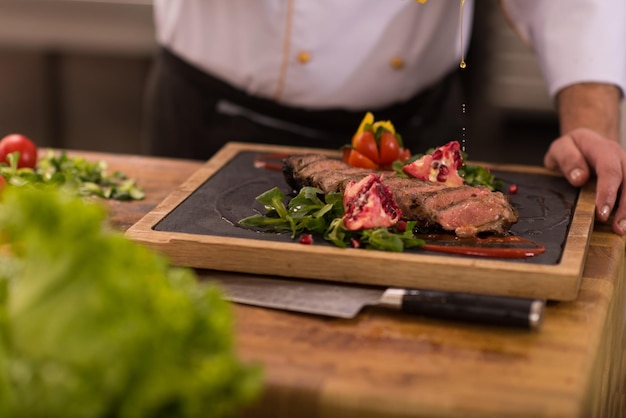 Chef terminando el plato de carne de bistec con finalmente aderezo y casi listo para servir en la mesa