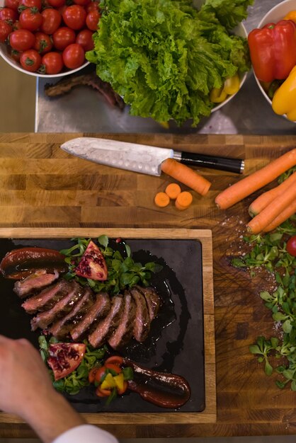 Foto chef terminando un plato de carne con finalmente aderezo para platos y casi listo para servir en la vista superior de la mesa