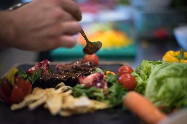 El chef terminó a mano el plato de carne de bistec con el aderezo para platos Finalmente y casi listo para servir en la mesa