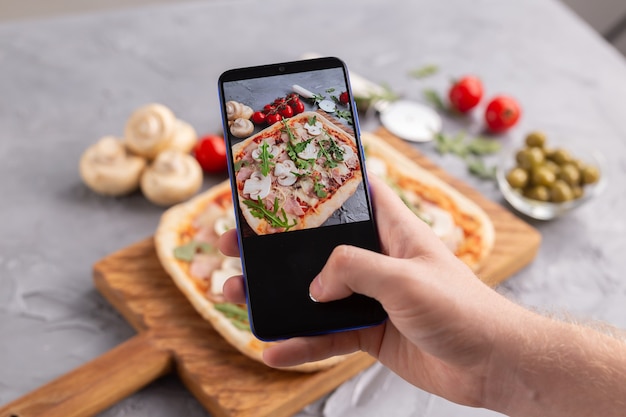 Chef tira fotos de pizza italiana cozida com presunto de parma em smartphone fotografando comida