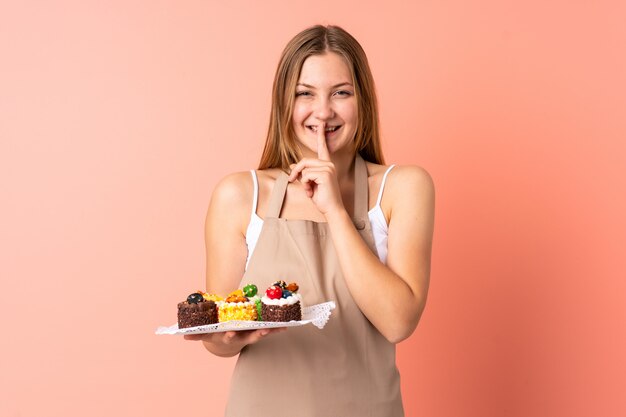 Chef ucraniano de pastelaria segurando um muffins isolado no rosa, fazendo o gesto de silêncio