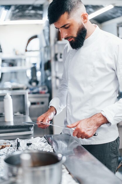 Chef en uniforme blanco de pie en la cocina sosteniendo cuchillos en las manos