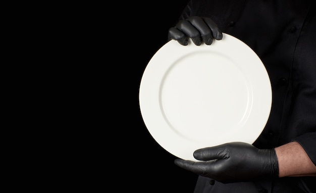 Chef en uniforme negro sosteniendo un plato vacío blanco redondo