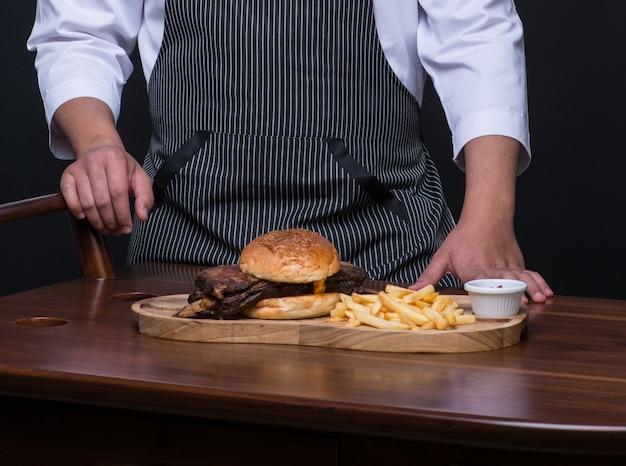 Chef uniformizado serve prato de carne em bandeja de madeira