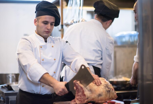 chef usando machado enquanto corta um grande pedaço de carne em uma placa de madeira na cozinha do restaurante