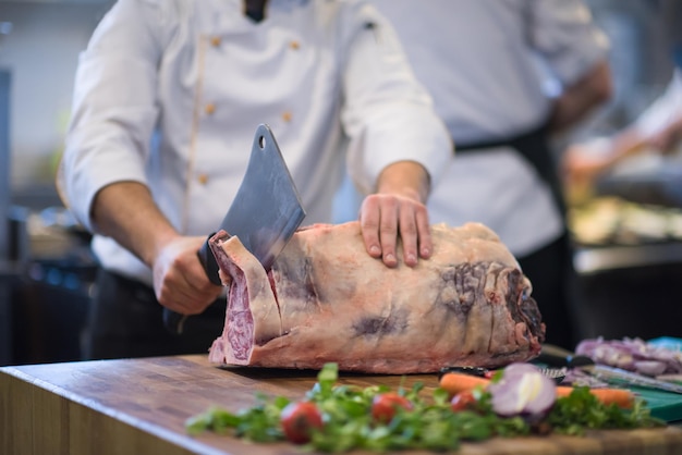 chef usando machado enquanto corta um grande pedaço de carne em uma placa de madeira na cozinha do restaurante