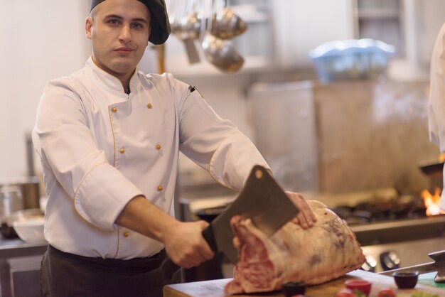 chef usando machado enquanto corta um grande pedaço de carne em uma placa de madeira na cozinha do restaurante