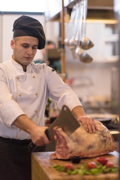 chef usando machado enquanto corta um grande pedaço de carne em uma placa de madeira na cozinha do restaurante