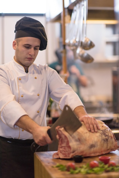 chef usando machado enquanto corta um grande pedaço de carne em uma placa de madeira na cozinha do restaurante