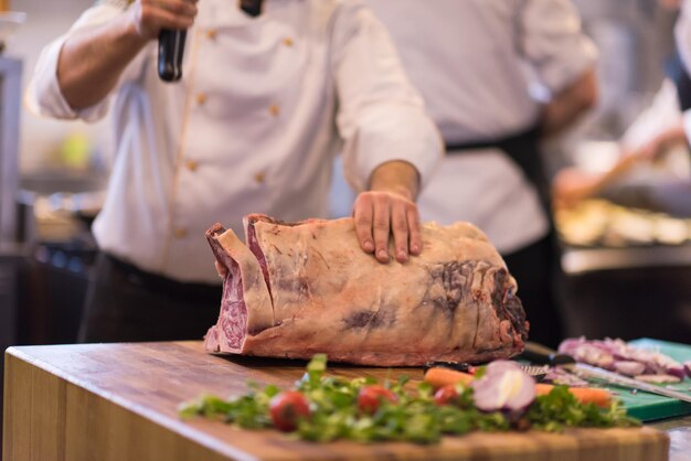 chef usando machado enquanto corta um grande pedaço de carne em uma placa de madeira na cozinha do restaurante