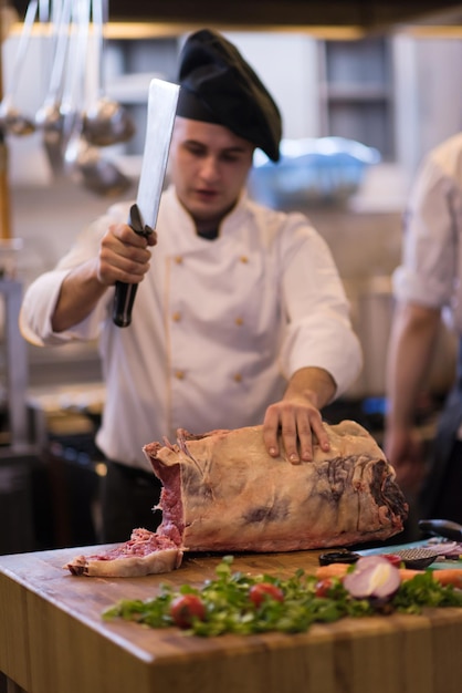 chef usando machado enquanto corta um grande pedaço de carne em uma placa de madeira na cozinha do restaurante