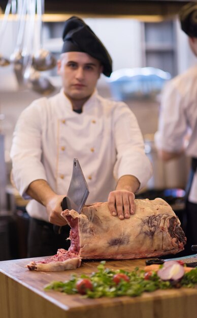 chef usando machado enquanto corta um grande pedaço de carne em uma placa de madeira na cozinha do restaurante