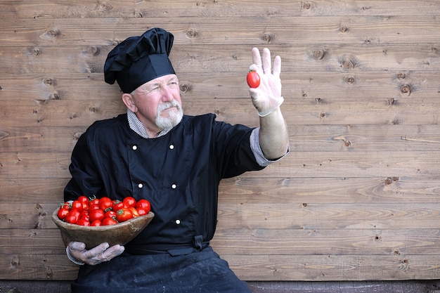 Chef velho de uniforme com legumes frescos em um bacground de madeira