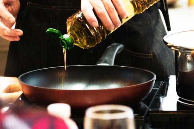 Chef vertiendo aceite en una sartén, Chef cocinando comida en la cocina