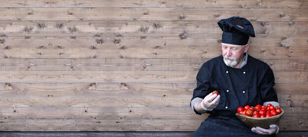 Chef viejo en uniforme con verduras frescas sobre un fundamento de madera