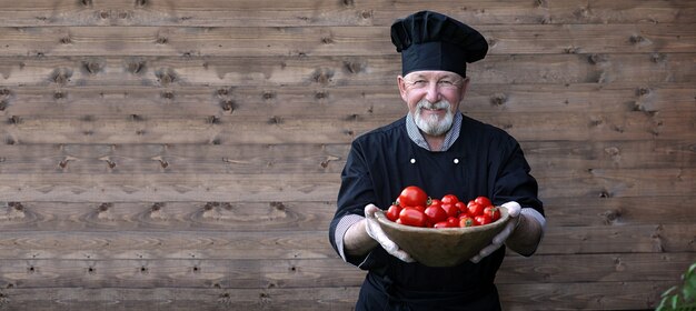 Chef viejo en uniforme con verduras frescas sobre un fundamento de madera