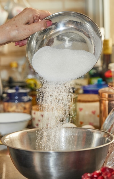 Foto el chef vierte azúcar en un bol para tarta de cerezas, clafoutis. receta paso a paso.