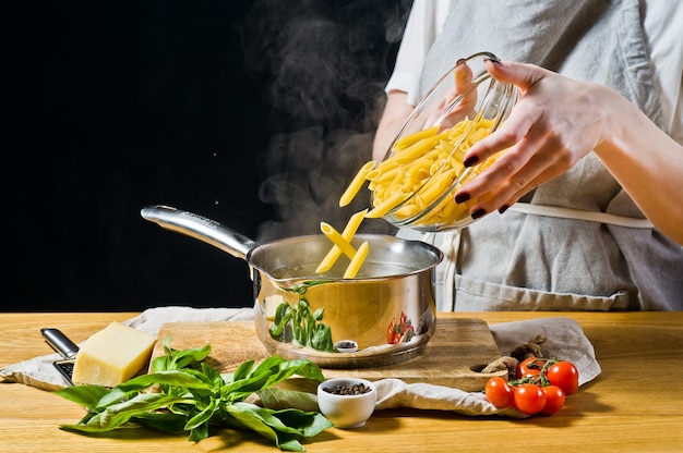 El chef vierte la pasta Penne en una olla con agua hirviendo.