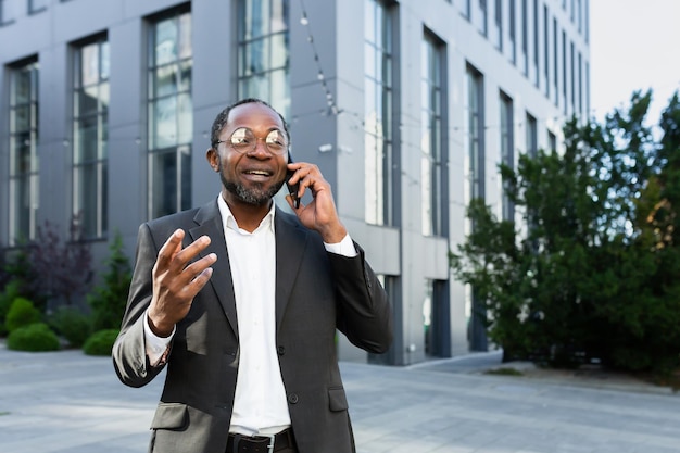 Chefe afro-americano alegre e satisfeito do lado de fora do prédio de escritórios sorrindo e conversando com