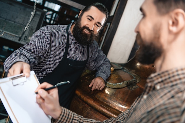 Chefe e trabalhador da cervejaria perto do tanque de aço inoxidável.