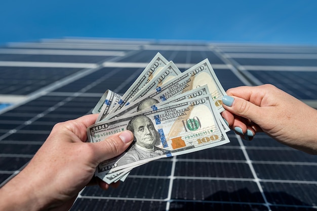 Foto chefe em uma jaqueta com mãos jovens recebe uma grande soma de dólares no contexto dos painéis solares conceito de eletricidade verde