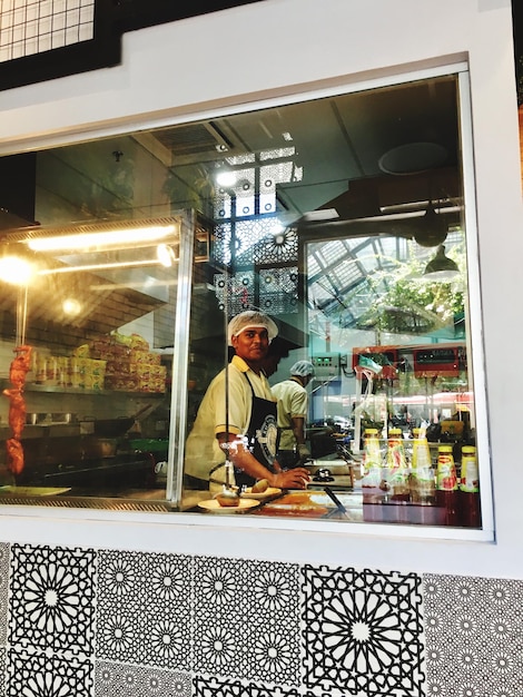 Foto chefe preparando comida na cozinha comercial vista através da janela