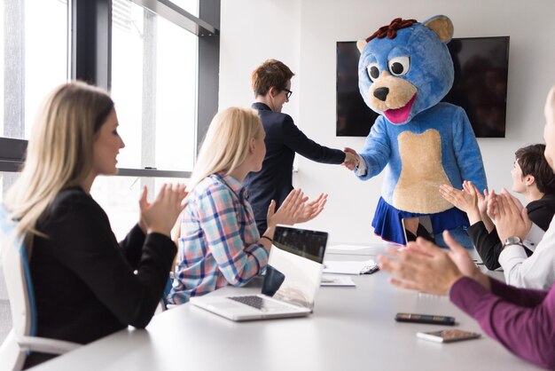 Chefe vestido como ursinho de pelúcia se divertindo com empresários no escritório corporativo moderno