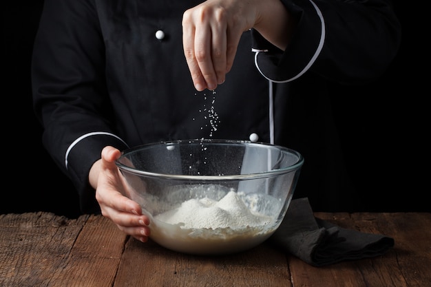 Chefhände besprüht Seesalz auf rohem Teig.