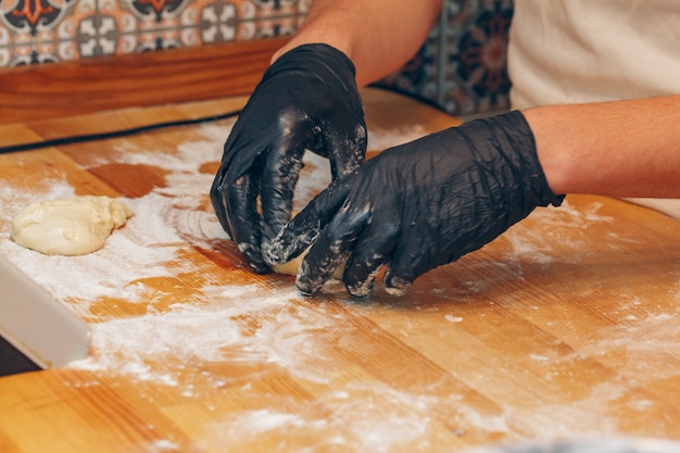 Chefhände in den schwarzen Handschuhen bereitet Teigabschluß oben zu