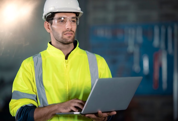 Chefingenieur im Schutzhelm geht durch leichte moderne Fabrik, während er Laptop hält