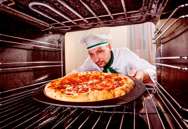 Chefkoch bereitet Peperoni-Pizza im Ofen zu, Blick aus dem Inneren des Ofens. Kochen im Ofen.