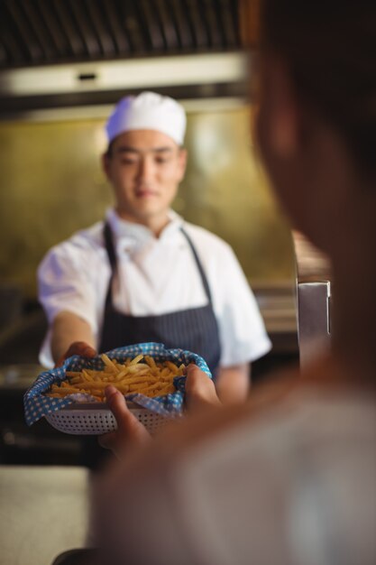 Chefkoch, der Tablett mit Pommes Frites zur Kellnerin übergibt