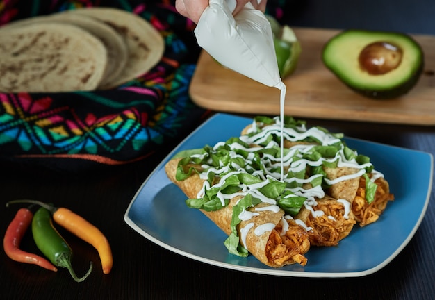 Chefkoch, der traditionellen schweren Sahneteller mit goldenen Tacos mit mexikanischem Essen mit Hühnchen platziert