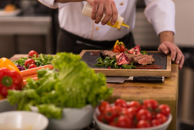 Chefkoch fertigt Steakfleischplatte mit Final Dish Dressing und ist fast servierfertig am Tisch