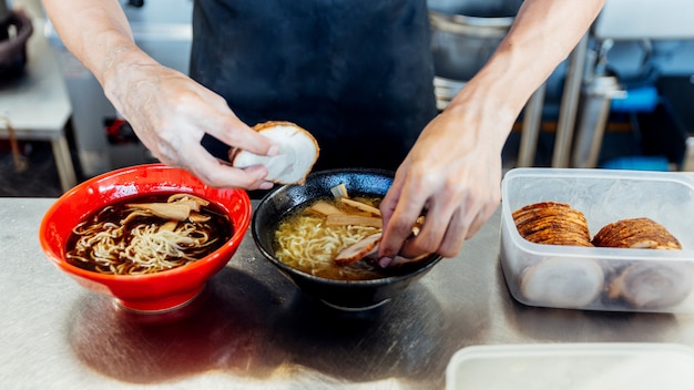 Chefkoch fügt Zutaten in Ramennudeln für die Herstellung von Miso und Shoyu Ramen hinzu.