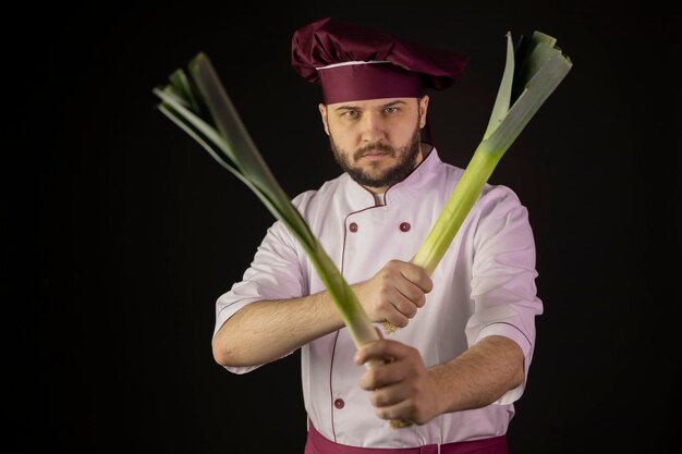 Chefkoch Mann in Uniform hält zwei Lauchstiele, die sie wie eine Waffe kreuzen