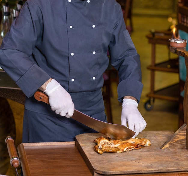 Chefkoch schneidet ein Hühnerfleisch mit einem Hackmesser auf dem Holzteller