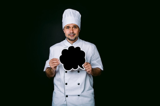 Foto chefkoch trägt kochjacke und hut, hält eine tafel mit comic-blasenrede, auf schwarzem hintergrund