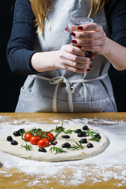 Chefkoch würzt rohe Foccacia. Draufsicht, hölzerner Hintergrund