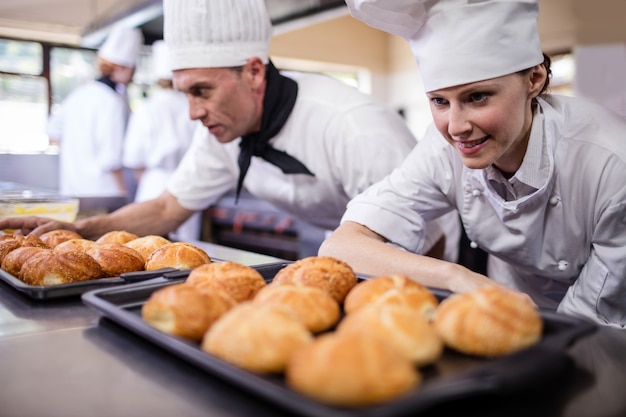 Chefs masculinos y femeninos preparando rollos de kaiser en la cocina