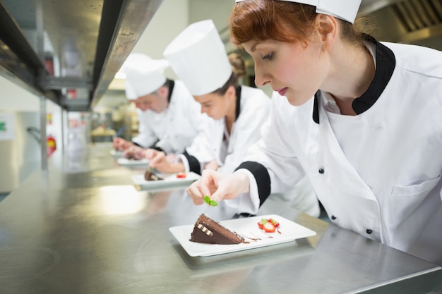 Foto chefs de pie en una fila adornando platos de postre