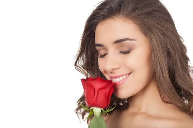 Cheirando uma rosa. Mulher jovem e bonita segurando uma rosa vermelha perto do nariz e mantendo os olhos fechados enquanto isolado no fundo branco