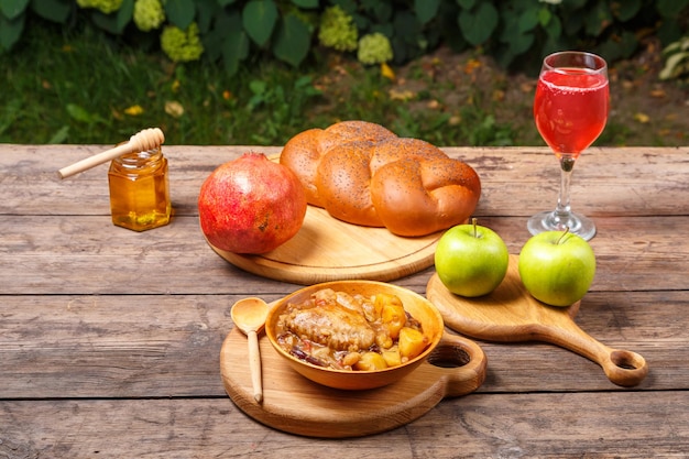 Chelnt mit Hähnchen in einem Holzteller mit einem Holzlöffel auf dem festlich gedeckten Tisch für Rosh Hashanah neben Challah-Honigwein