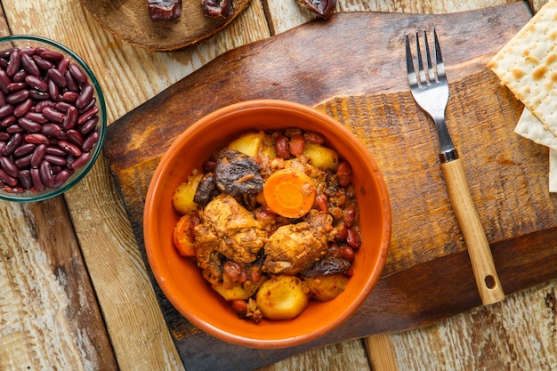 Chelnt prato judeu com carne na mesa em um prato em um suporte ao lado dos ingredientes e pão ázimo.