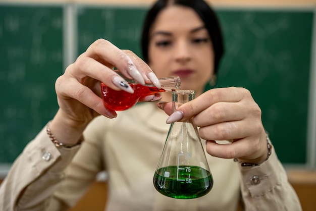 Chemie-Lehrerin beobachtet Reaktionsteströhrchen im Klassenzimmer und gegen grüne Tafel