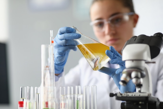 Chemikerin hält Flasche mit gelber Flüssigkeit in ihren Händen im chemischen Labor