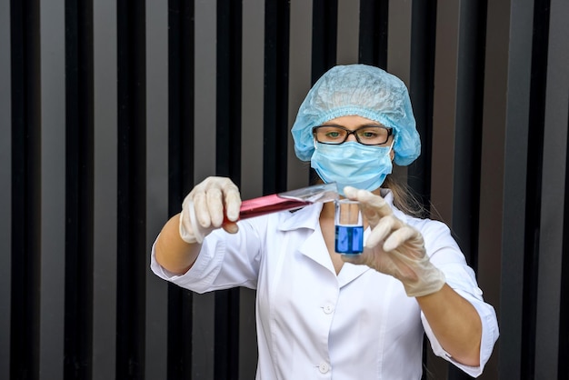 Chemikerin macht Experiment mit Reagenzglas und Flasche mit medizinischem Mantel und Maske