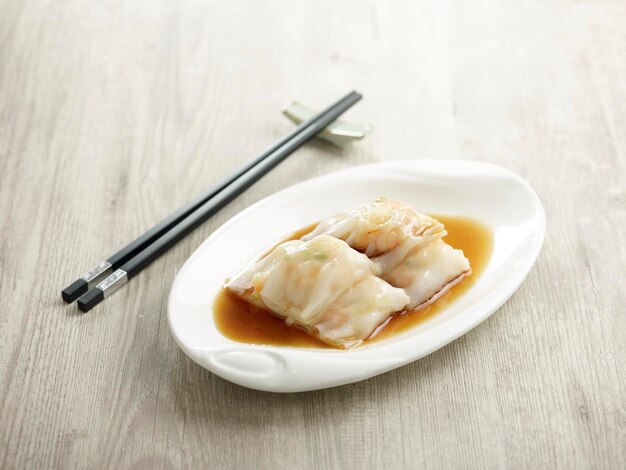 Cheongfun al vapor con relleno de gambas frescas servido en un plato aislado en la vista lateral de la tabla de cortar sobre fondo oscuro