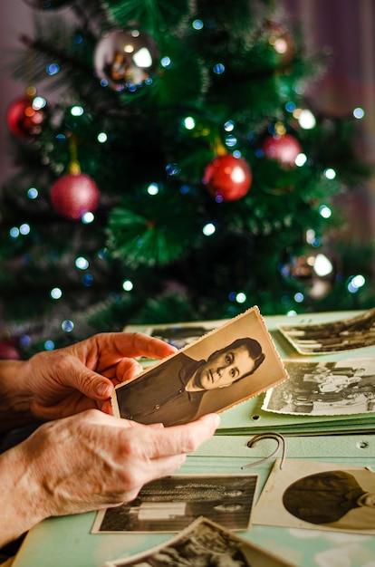 Cherkasy / Ucrania - 12 de diciembre de 2019: Manos femeninas sosteniendo una foto de su madre en el fondo del árbol de Navidad